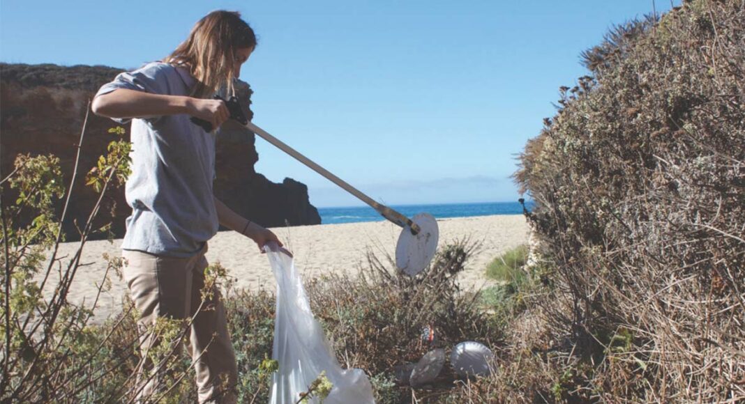 Volunteer Abby Herring fills up a garbage bag with trash left over from beachgoers at Panther Beach