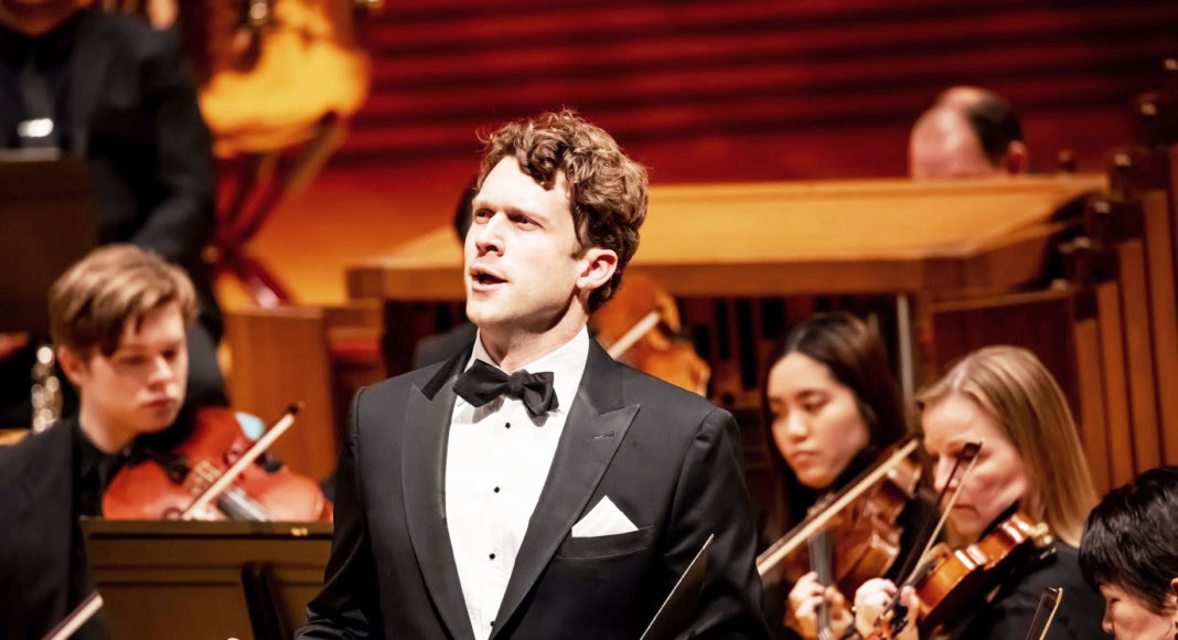 Handsome young man singing with orchestra musicians in the background