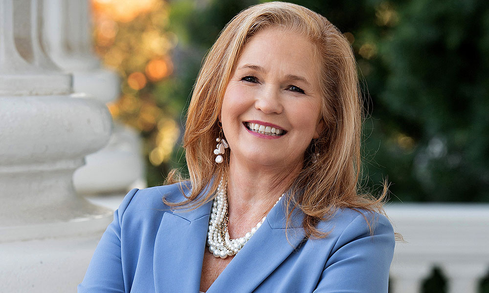 Blond woman wearing a jacket and pearls, photographed outdoors