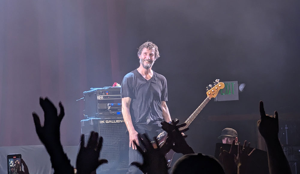 Man playing guitar on stage in front of an audience with raised hands