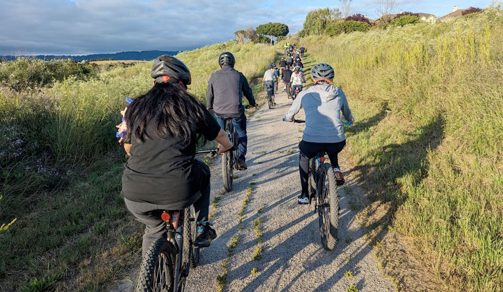 Group of cyclists riding on a trail through open space, seen from behind