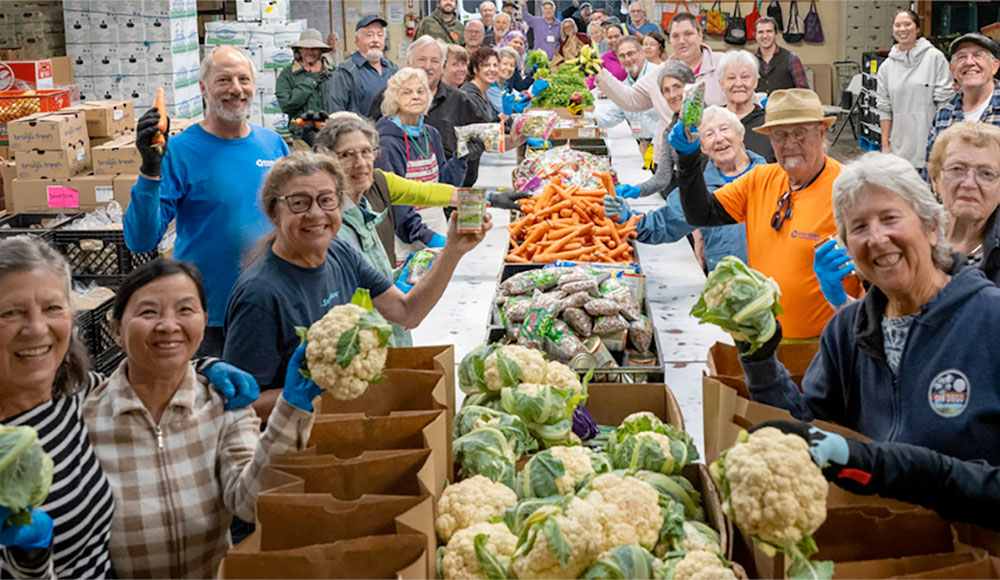 Group of people lined up on both sides of a long table covered with vegetables