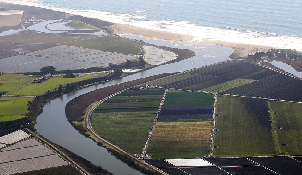Aerial view of a river flowing into the ocean, and surrounding farmlands