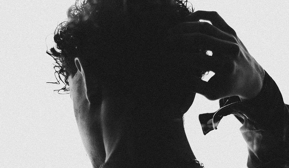 Man photographed from behind in silhouette, putting his hand on his head