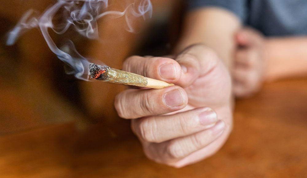 Outstretched hand leaning on a table and holding a lit joint