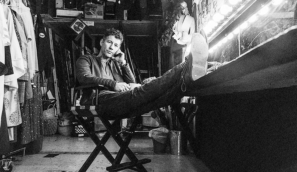 Black-and-white photo of a guy backstage with his feet propped up