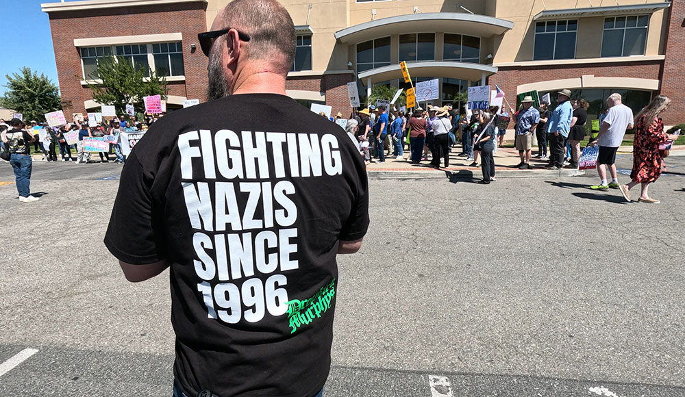 Man at a rally wearing a shirt that says “Fighting Nazis Since 1996”