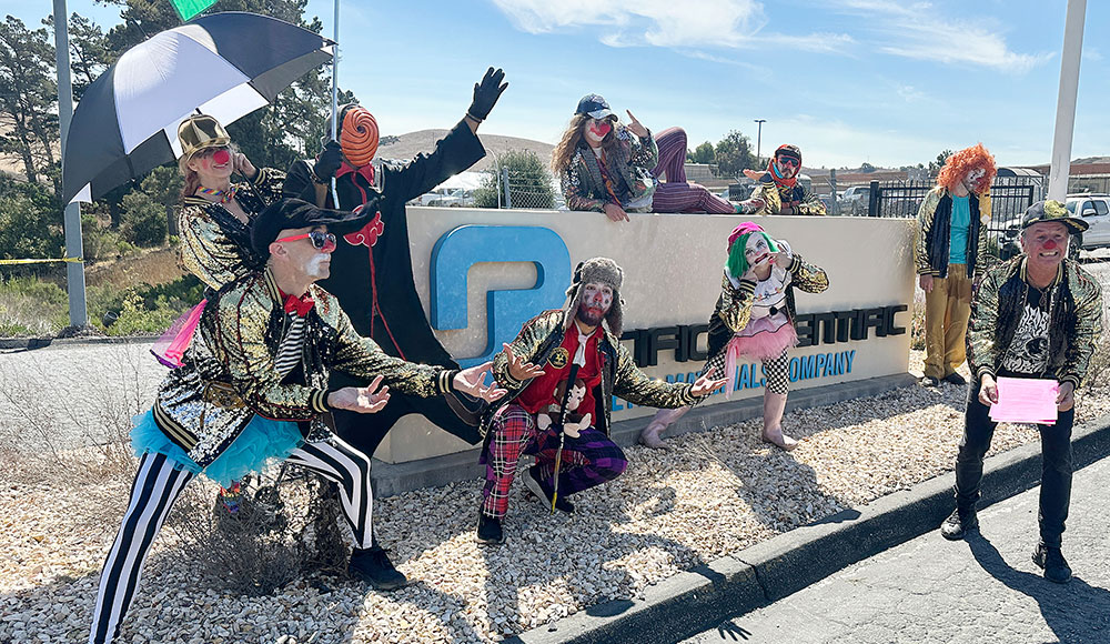 Several people in clown costumes congregate around the main entrance of a company