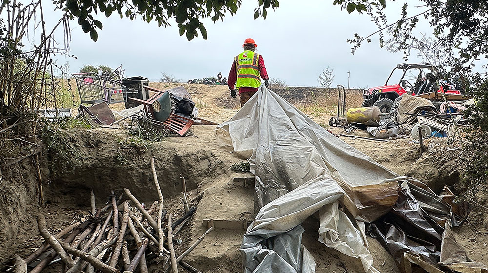 NEWS photo A worker hauls a tarp out of a homeless camp.