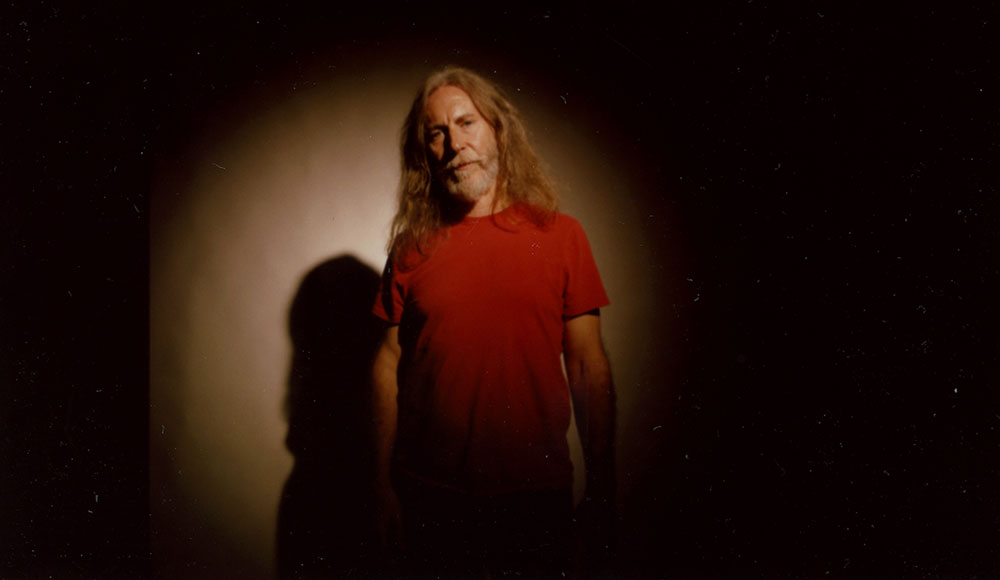 Man against a black background wearing a red shirt with a light shining on him