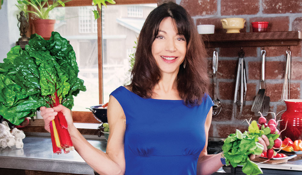 Woman in a kitchen holding up fresh produce