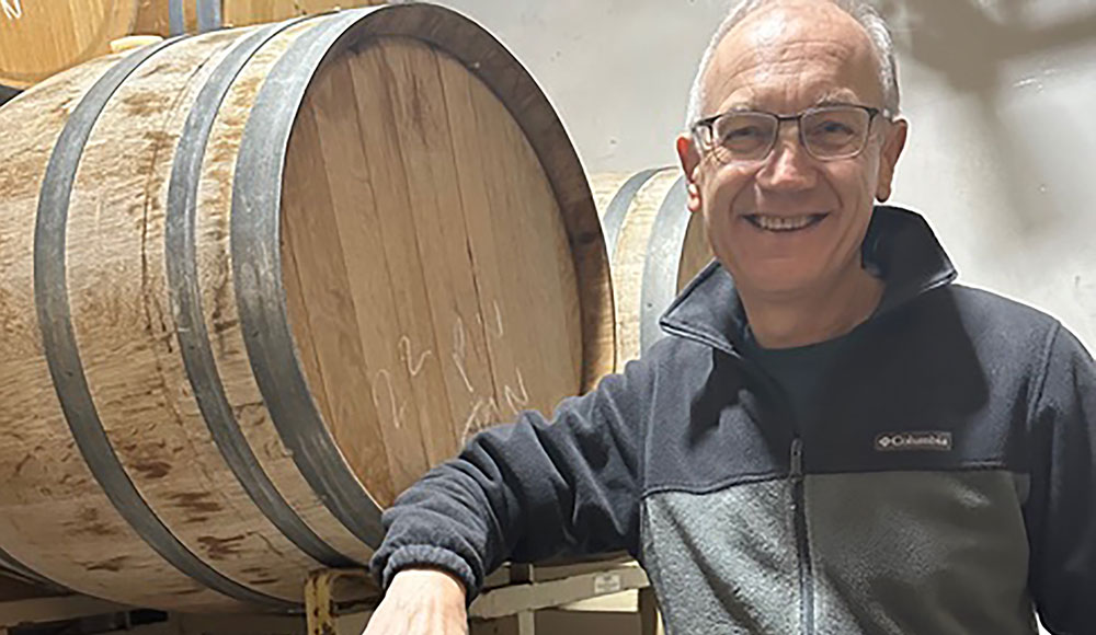 Winemaker Tony Craig dressed casually in a dark hoodieposes with a wine barrel