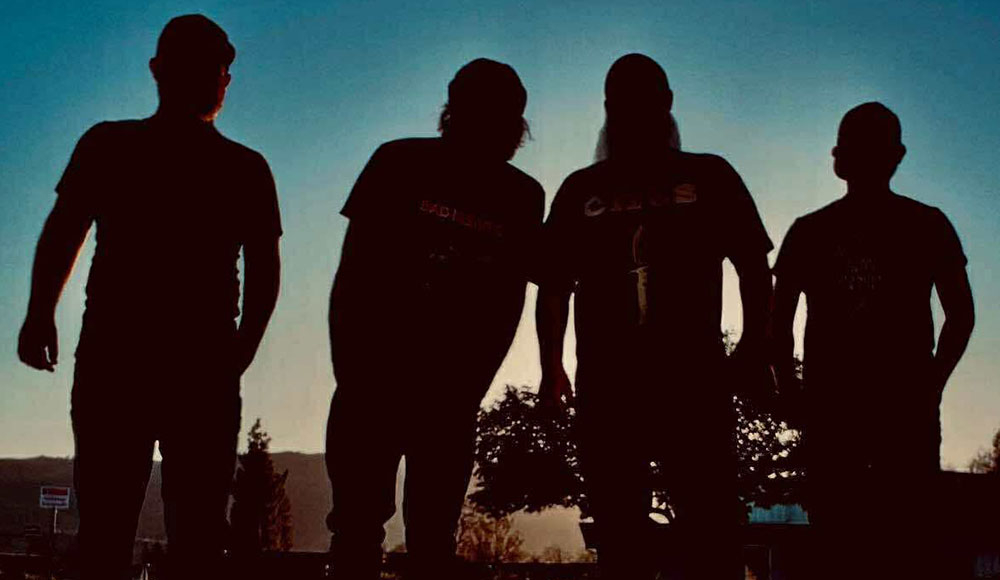 Silhouetted photo of the four members of the rock band Drawing Heaven standing against a dusky blue sky.