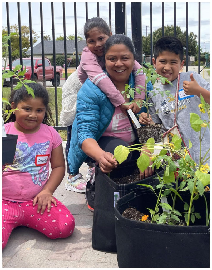 A smiling woman and three children plant vegetables together in portable grow bags during a Monterey Bay Master Gardeners workshop.