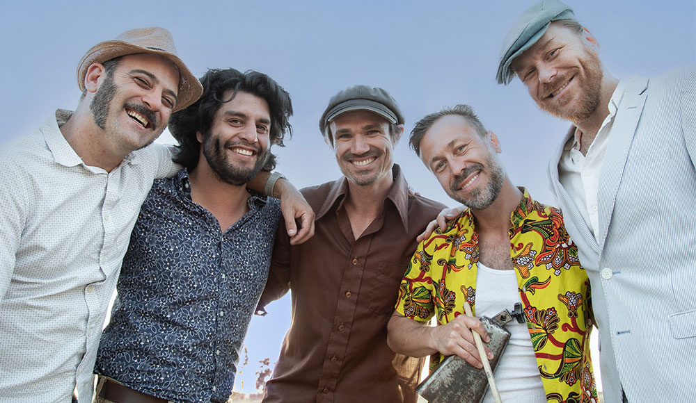 The California Honeydrops band members stand together smiling outdoors, arms around each other.