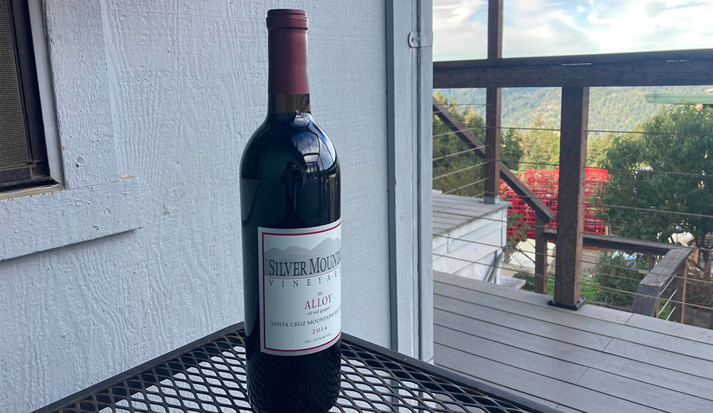 A bottle of Silver Mountain Vineyards Alloy wine on an outdoor table overlooking a mountain view.