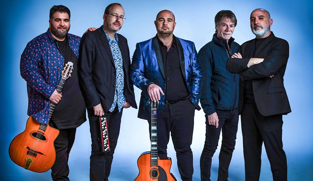 The Django Festival Allstars stand together holding guitars, posing against a light blue studio background.
