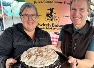 Switch It Up A smiling woman and man hold a chocolate layer cake with chai meringue at the Switch Bakery booth at a local farmers market.