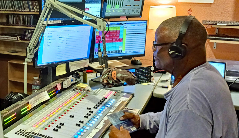 Man hosting a live radio show at KSQD, sitting at a control board with headphones on.
